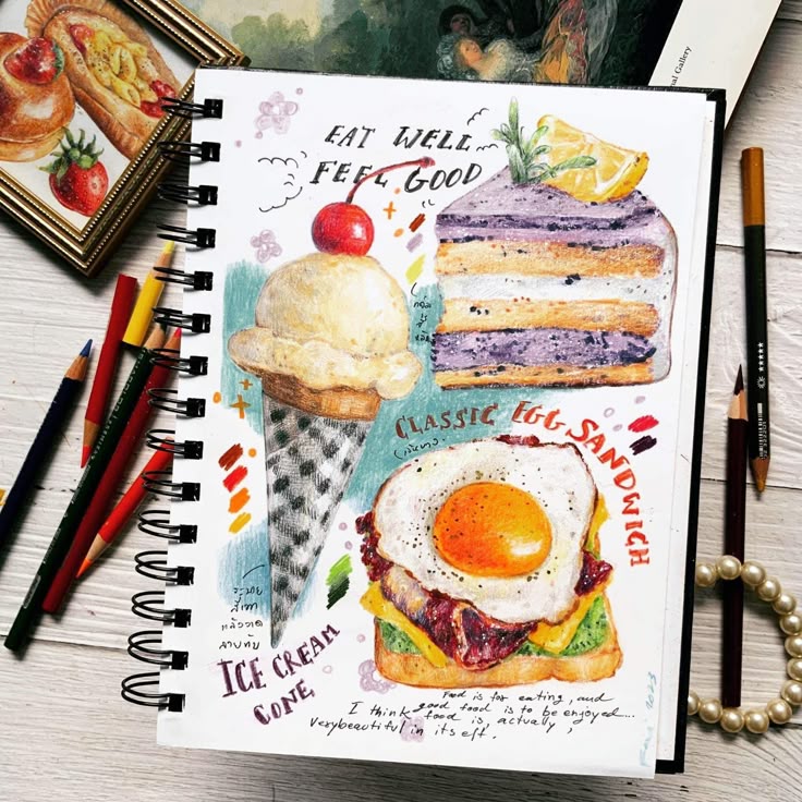 Hand-drawn food illustration with ice cream, cake, and egg sandwich in a sketchbook with colored pencils nearby.