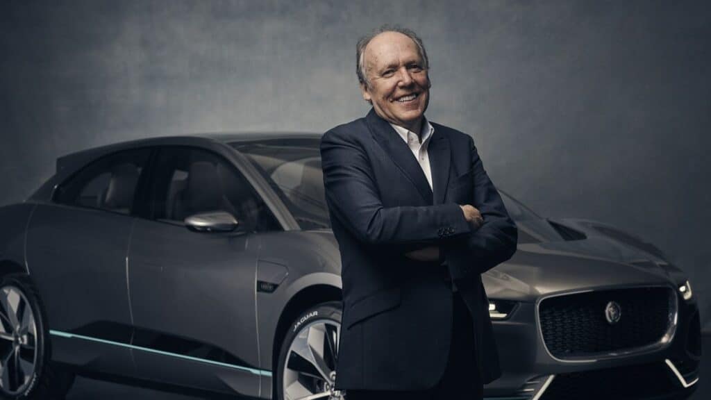 Man in suit smiling with a luxury car in the background, conveying confidence and style.