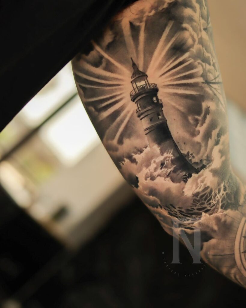 Arm tattoo featuring a detailed lighthouse surrounded by clouds and rays of light, highlighting skillful shading.
