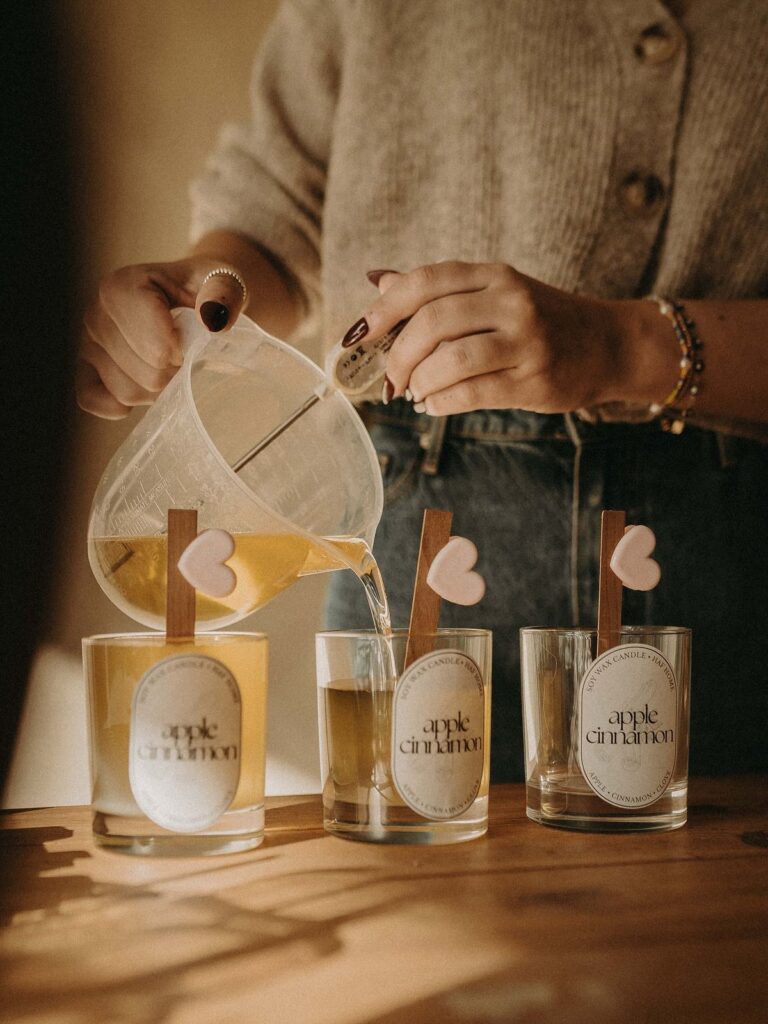 e9965f0a6e1d52401f44d5ac70e03933 Person pouring wax into apple cinnamon candles with heart-shaped wicks on wooden table. | Sky Rye Design Person pouring wax into apple cinnamon candles with heart-shaped wicks on wooden table.