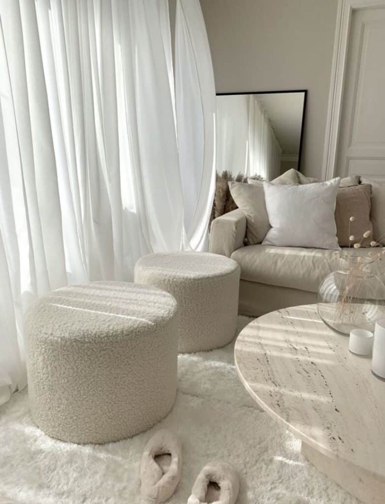 eb37e1e9a41717888cf00fd466cbe2f7 Cozy neutral living room with plush stools, a beige sofa, shearling slippers, and soft natural light from large windows. | Sky Rye Design Cozy neutral living room with plush stools, a beige sofa, shearling slippers, and soft natural light from large windows.