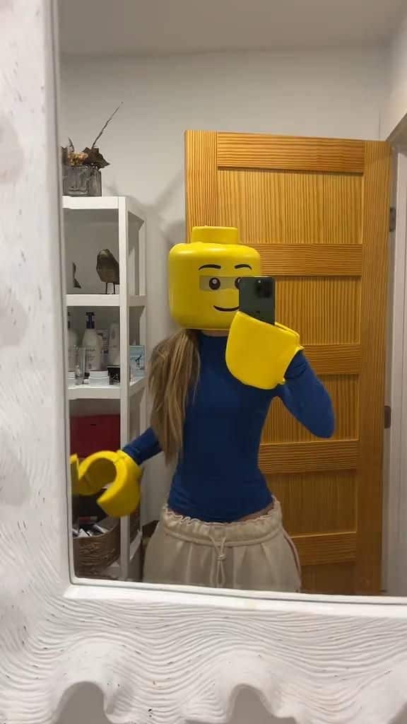 Person in a LEGO costume taking a mirror selfie in a bathroom.