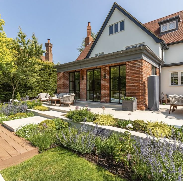 ec5948ef-7d3d-4be1-8ed4-97eaa348ab59 Modern brick house with a lush garden and patio furniture, under a clear blue sky. | Sky Rye Design Modern brick house with a lush garden and patio furniture, under a clear blue sky.