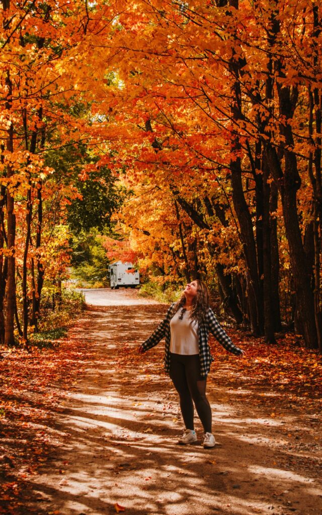 Woman enjoying a walk on an autumn path lined with vibrant orange and yellow trees.