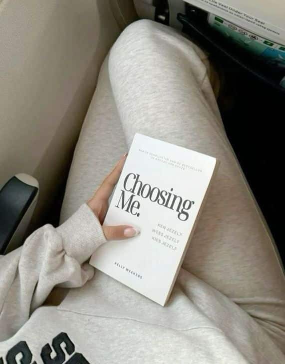 ecf5cc2c-c23b-44b2-b382-b35d03f9bf4a Person in grey loungewear holding Choosing Me book on their lap while sitting on an airplane seat. | Sky Rye Design Person in grey loungewear holding Choosing Me book on their lap while sitting on an airplane seat.