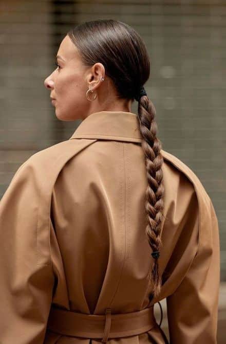 Woman with braided hair wearing tan coat, viewed from behind.