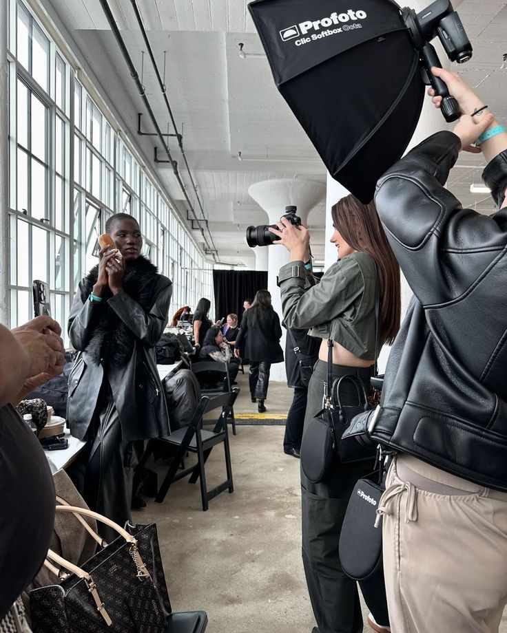 Photographer capturing backstage fashion show moments, with model posing in stylish outfit and accessories.