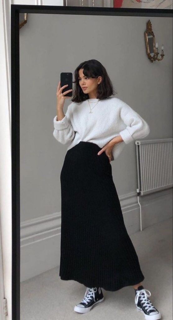ee21b83f-e128-4324-86f8-a21377a69618 Woman in white sweater and black skirt takes mirror selfie, wearing black Converse sneakers. Fashionable and casual look. | Sky Rye Design Woman in white sweater and black skirt takes mirror selfie, wearing black Converse sneakers. Fashionable and casual look.