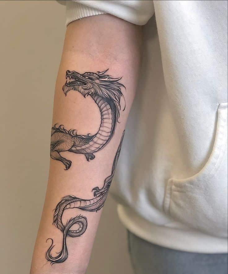 Intricate dragon tattoo on forearm, showcasing detailed scales and flowing design, against a white hoodie backdrop.