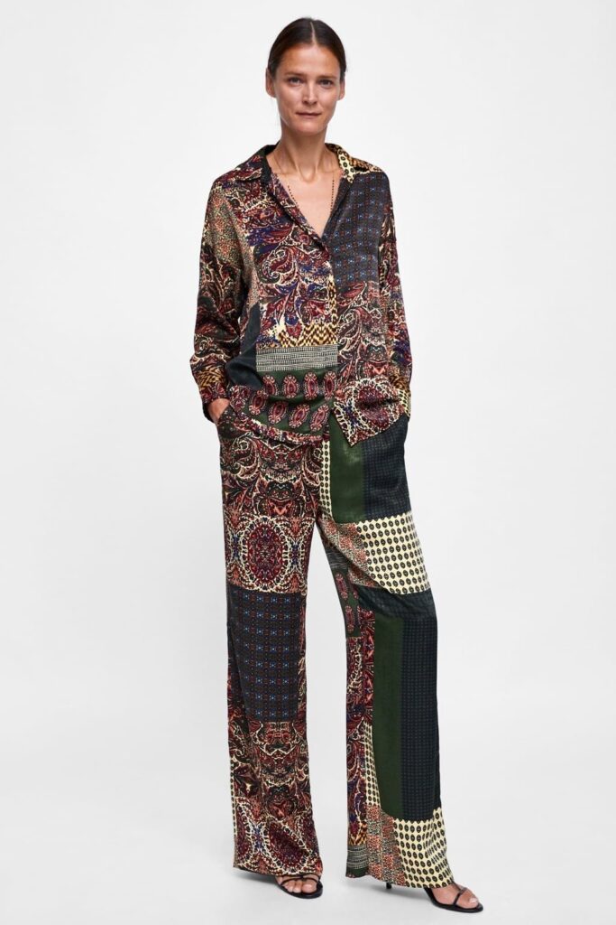 ef971864fcbab0eb1ab91fa2a479d16a Woman in a colorful patchwork outfit standing against a white background, hands in pockets, wearing sandals. | Sky Rye Design Woman in a colorful patchwork outfit standing against a white background, hands in pockets, wearing sandals.