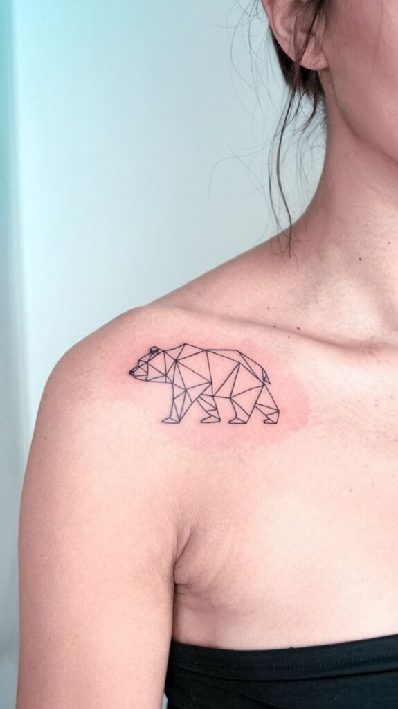 Geometric bear tattoo on woman's shoulder, minimalist line art design on skin.