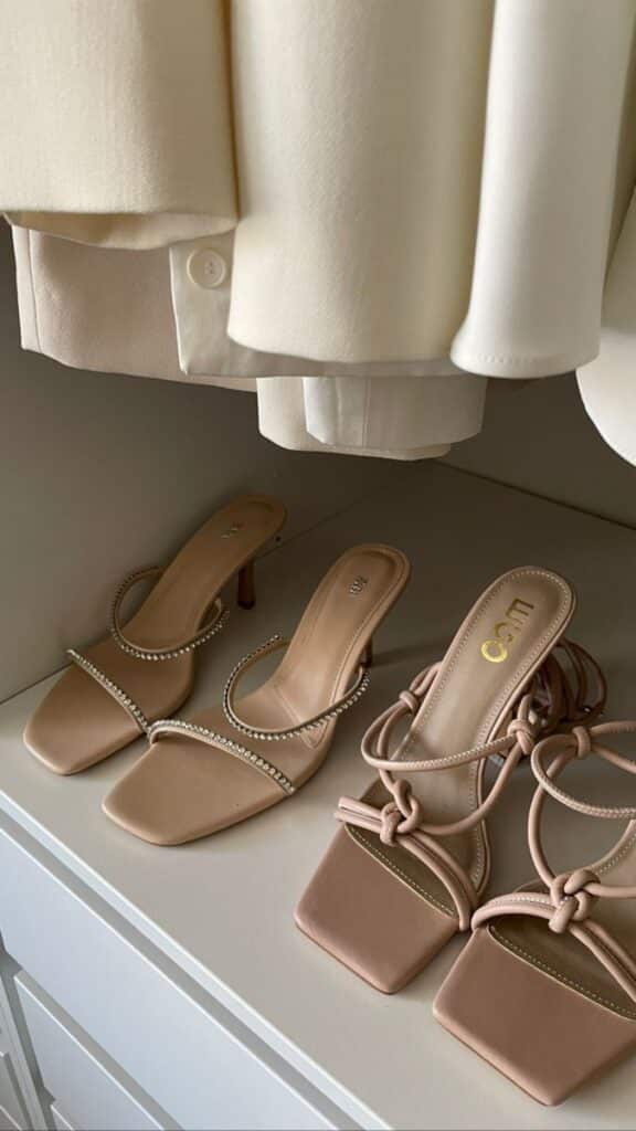 erika fane _ corrupt Elegant beige high-heeled sandals with chic designs on a closet shelf under cream-colored clothing. | Sky Rye Design Elegant beige high-heeled sandals with chic designs on a closet shelf under cream-colored clothing.