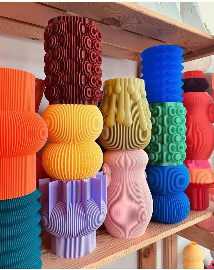 Colorful, modern vases with textured patterns stacked on a wooden shelf, showcasing vibrant home decor options.