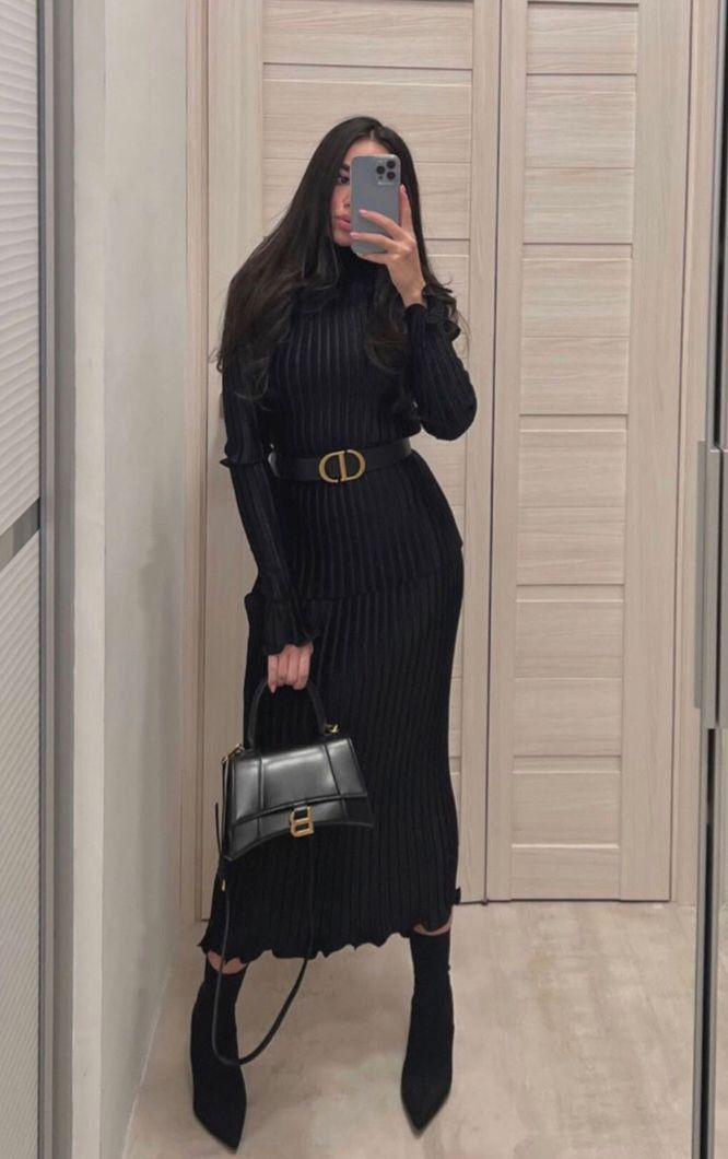 Woman in black ribbed dress with belt and handbag taking a mirror selfie in elegant outfit.