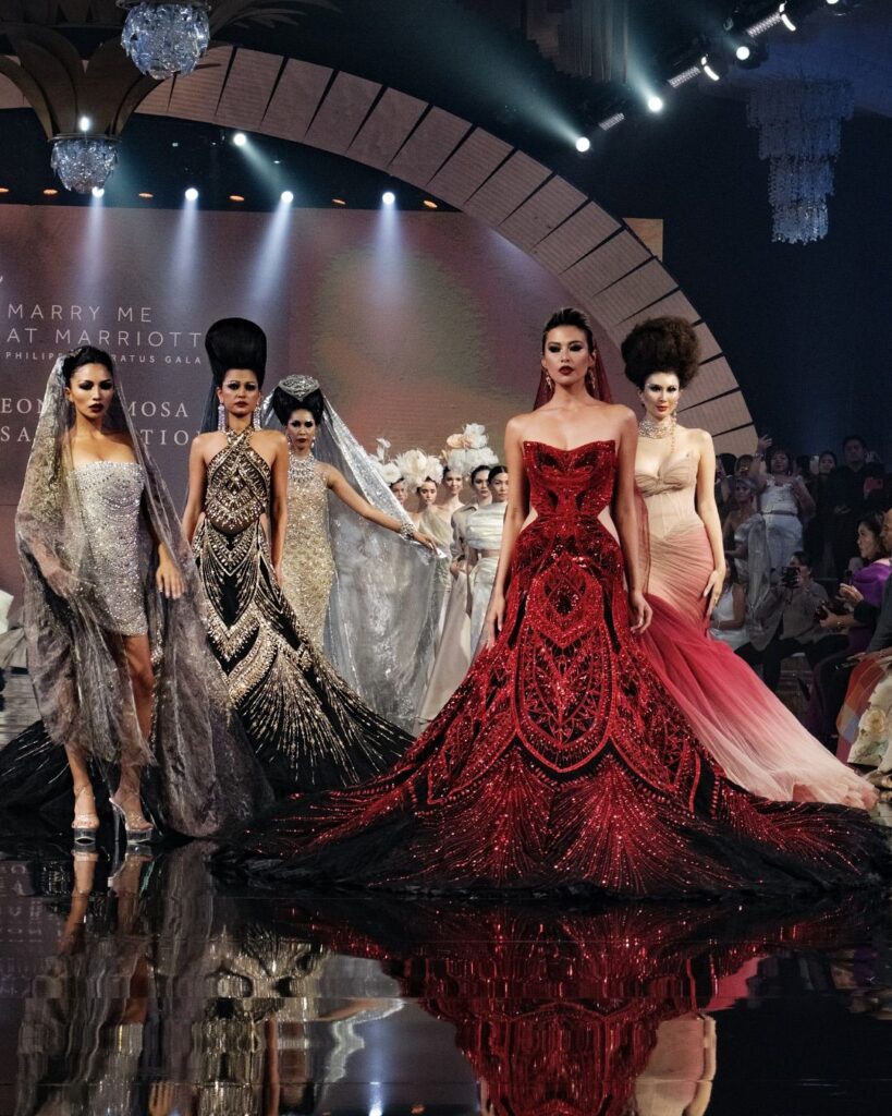 Fashion models showcase elegant gowns on a runway at a glamorous event.
