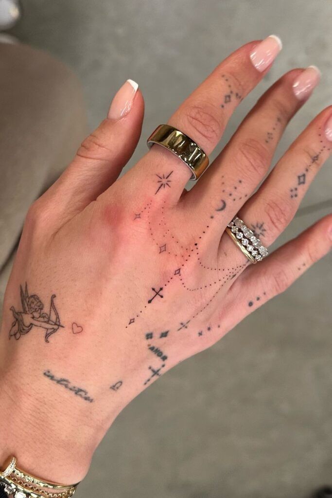 fa14031d0915c23e166d5267938c1426 Hand with delicate tattoos and rings, featuring celestial designs and a cherub, showcasing minimalist tattoo art. | Sky Rye Design Hand with delicate tattoos and rings, featuring celestial designs and a cherub, showcasing minimalist tattoo art.