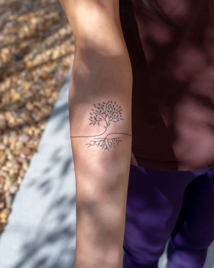 Simple tree tattoo on forearm with branches and roots, symbolizing growth and stability in minimalistic black ink.