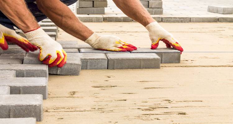 fitting-brick-stone-steps-cost-5-c2m800 Worker laying paving stones on sand, wearing gloves. | Sky Rye Design Worker laying paving stones on sand, wearing gloves.