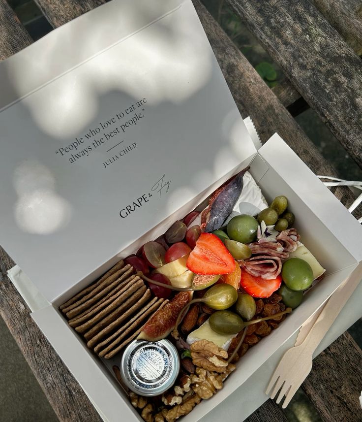 grape fig london Gourmet picnic box with cheese, fruits, olives, crackers, and a wooden fork on a rustic bench. | Sky Rye Design Gourmet picnic box with cheese, fruits, olives, crackers, and a wooden fork on a rustic bench.