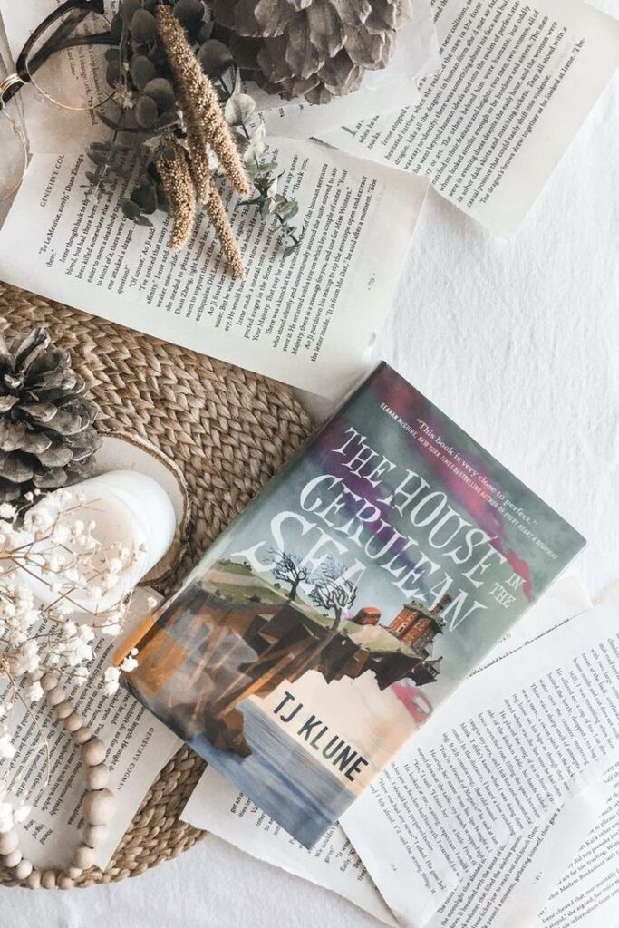 h o l l a Cozy flatlay with The House in the Cerulean Sea book, dried flowers, and decorative items on a woven mat. | Sky Rye Design Cozy flatlay with The House in the Cerulean Sea book, dried flowers, and decorative items on a woven mat.