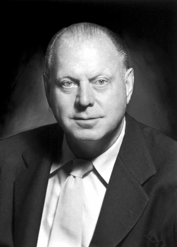 Black and white portrait of a man in a suit and tie with a neutral expression.