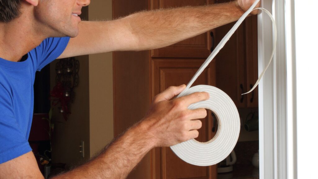 how-to-apply-weatherstripping Person applying weatherstripping tape to a door frame for insulation in a home improvement project. | Sky Rye Design Person applying weatherstripping tape to a door frame for insulation in a home improvement project.