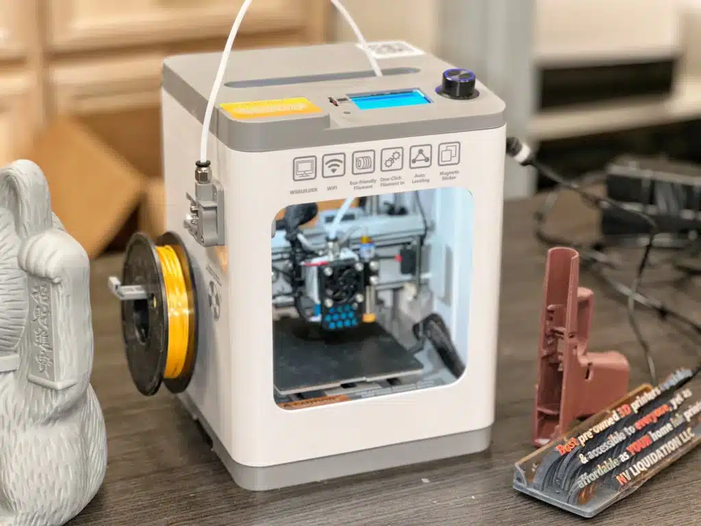 Compact 3D printer with yellow filament spool, flanked by printed models on a workspace table.