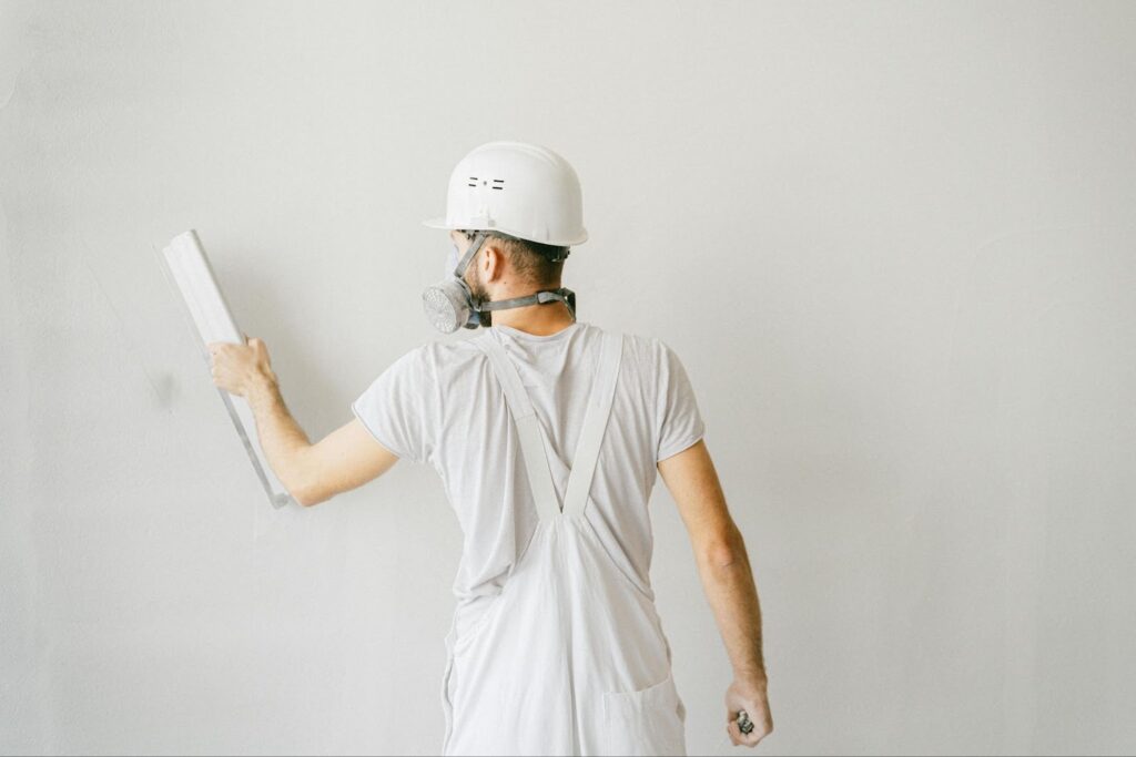 image Construction worker in white overalls and hard hat plastering a wall, ensuring smooth surface finish. | Sky Rye Design Construction worker in white overalls and hard hat plastering a wall, ensuring smooth surface finish.