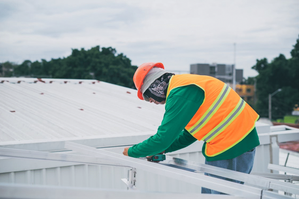 Construction worker in high-visibility vest and helmet working on a metal structure outdoors.