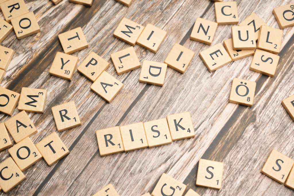 Scrabble tiles on a wooden surface spelling RISK among scattered letters, symbolizing unpredictability.