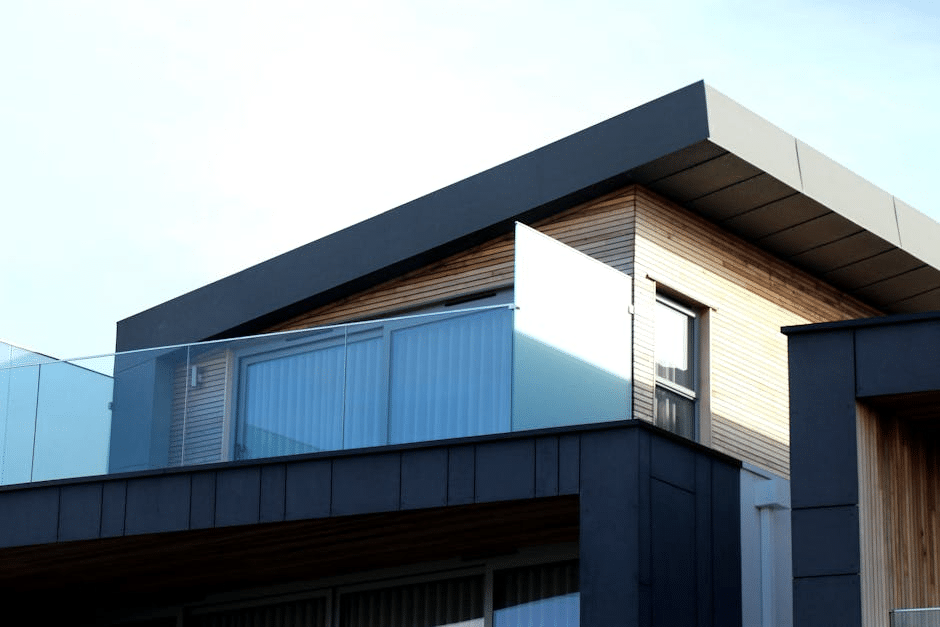 Modern house exterior with glass balcony and sleek architectural design against clear sky.