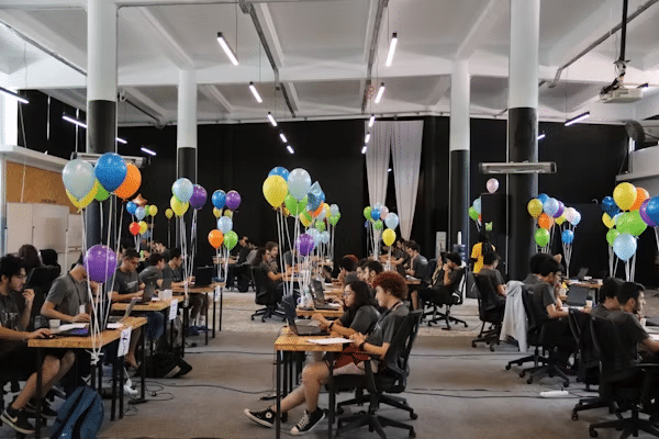 image Hackathon participants working at tables, surrounded by colorful balloons in a spacious, well-lit room. | Sky Rye Design Hackathon participants working at tables, surrounded by colorful balloons in a spacious, well-lit room.