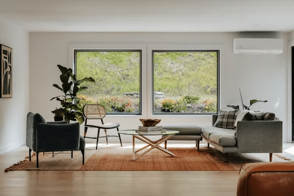 image Modern living room with large windows showcasing a garden view, featuring a cozy sofa, chairs, and indoor plants. | Sky Rye Design Modern living room with large windows showcasing a garden view, featuring a cozy sofa, chairs, and indoor plants.