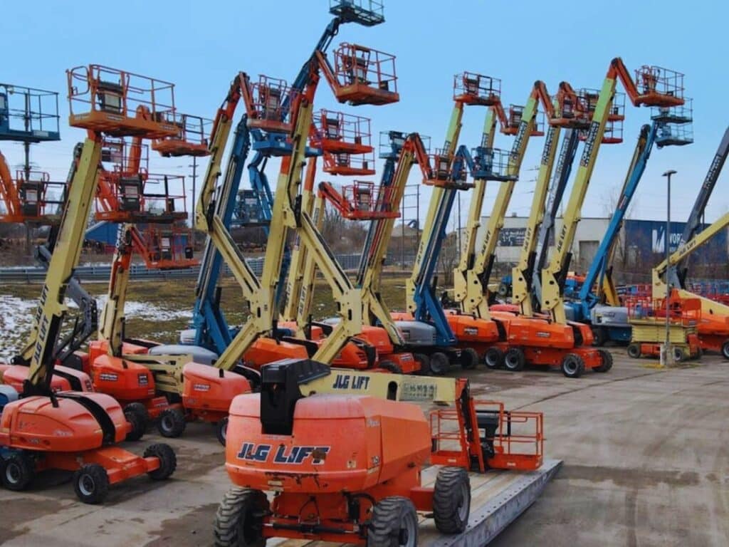 A row of orange and yellow boom lifts in an outdoor lot, ready for construction use under a clear blue sky.
