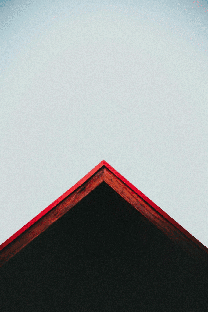 Close-up of a red roof peak against a clear sky, showcasing minimalist architectural design.