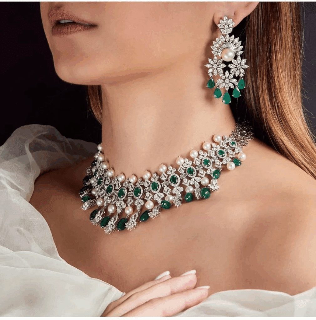 Woman wearing an elegant jewelry set with emeralds, pearls, and diamonds, including earrings and a necklace.
