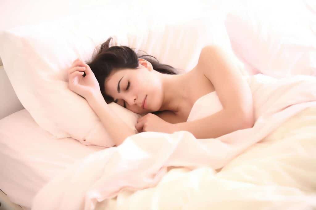 image Woman peacefully sleeping in white bed, surrounded by cozy pillows and soft sheets. | Sky Rye Design Woman peacefully sleeping in white bed, surrounded by cozy pillows and soft sheets.