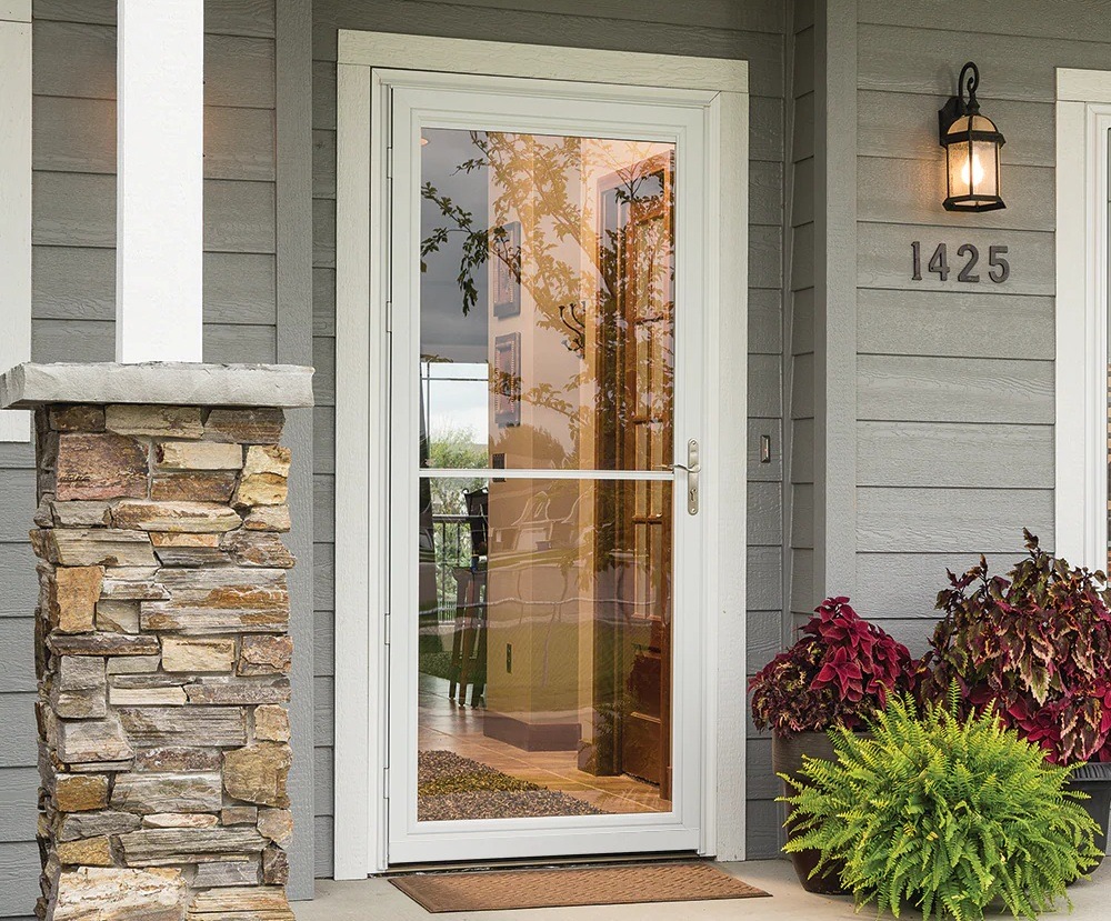 image Modern gray house exterior with stone pillar, glass storm door, outdoor light, and vibrant plants by entrance. | Sky Rye Design Modern gray house exterior with stone pillar, glass storm door, outdoor light, and vibrant plants by entrance.