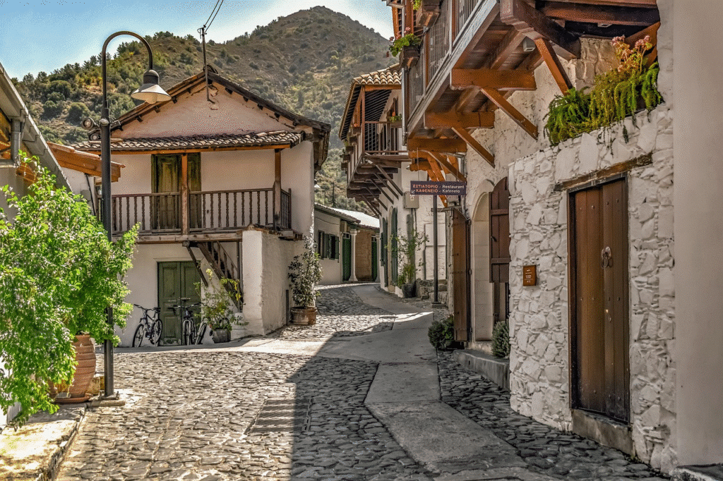 Charming cobblestone street in a Mediterranean village with rustic buildings and mountain backdrop.