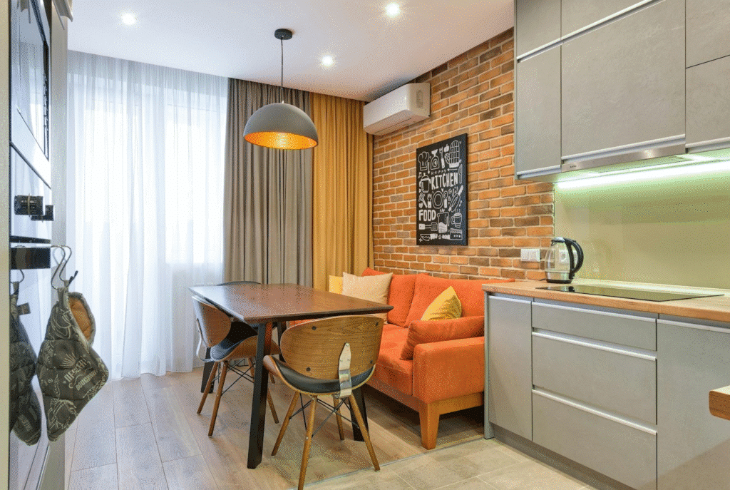 image Modern kitchen with brick wall, cozy orange sofa, wooden table, and pendant lighting. | Sky Rye Design Modern kitchen with brick wall, cozy orange sofa, wooden table, and pendant lighting.