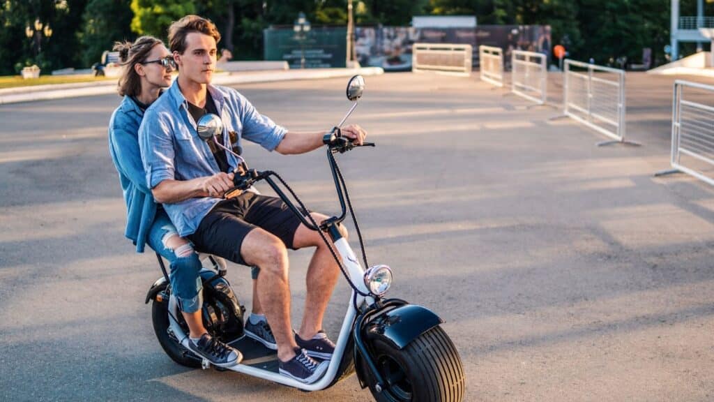 image Couple riding an electric scooter on a sunny day in a park, enjoying a leisurely ride together. | Sky Rye Design Couple riding an electric scooter on a sunny day in a park, enjoying a leisurely ride together.