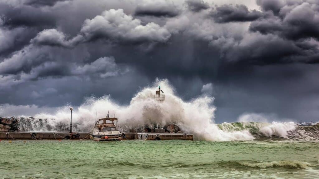 image Stormy sea waves crash against a pier, with a lighthouse and boat, under a dramatic cloudy sky. | Sky Rye Design Stormy sea waves crash against a pier, with a lighthouse and boat, under a dramatic cloudy sky.