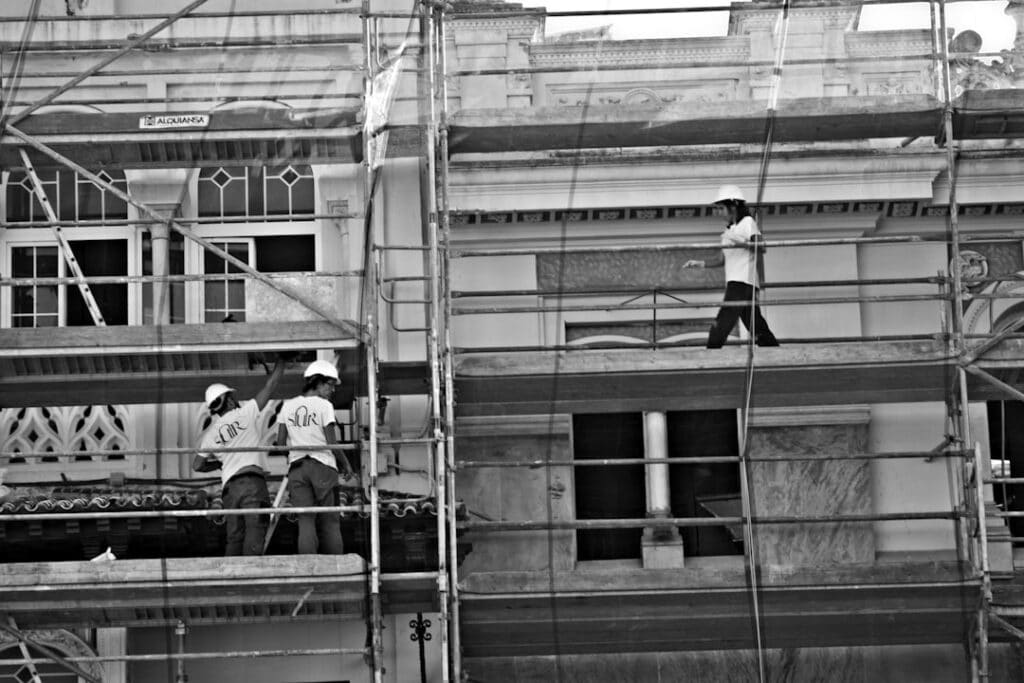 image Construction workers on scaffolding renovating a building facade in black and white. | Sky Rye Design Construction workers on scaffolding renovating a building facade in black and white.