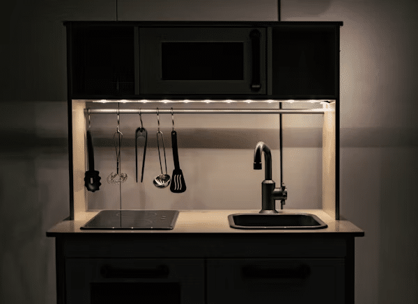 Modern kitchen with hanging utensils, sleek faucet, stovetop, and microwave under cabinet lighting.