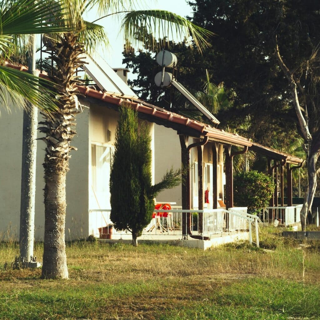 image Single-story house with solar panels, surrounded by palm trees and grass, under a clear sky. | Sky Rye Design Single-story house with solar panels, surrounded by palm trees and grass, under a clear sky.