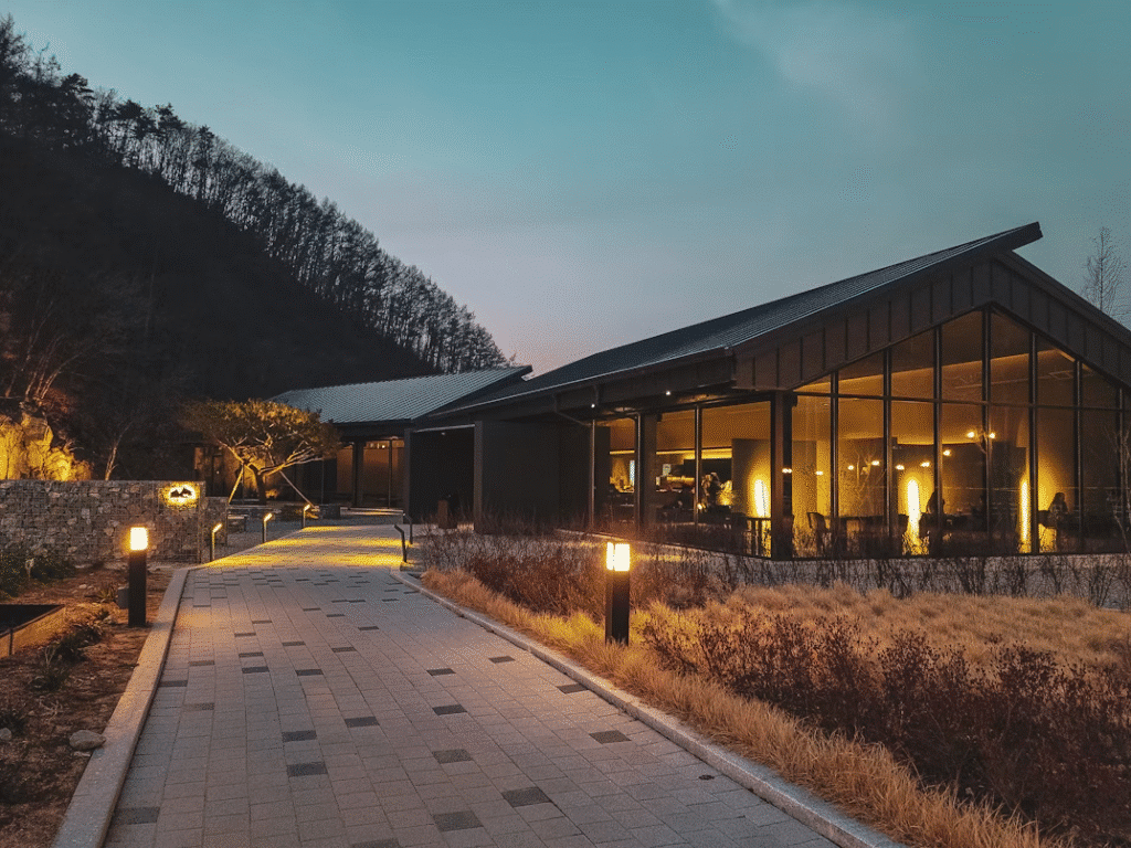 image Modern building with large windows at dusk, surrounded by a lit pathway and trees under a tranquil evening sky. | Sky Rye Design Modern building with large windows at dusk, surrounded by a lit pathway and trees under a tranquil evening sky.