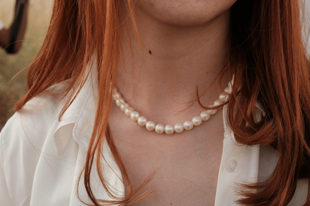 image Red-haired woman wearing a pearl necklace and white blouse outdoors. | Sky Rye Design Red-haired woman wearing a pearl necklace and white blouse outdoors.