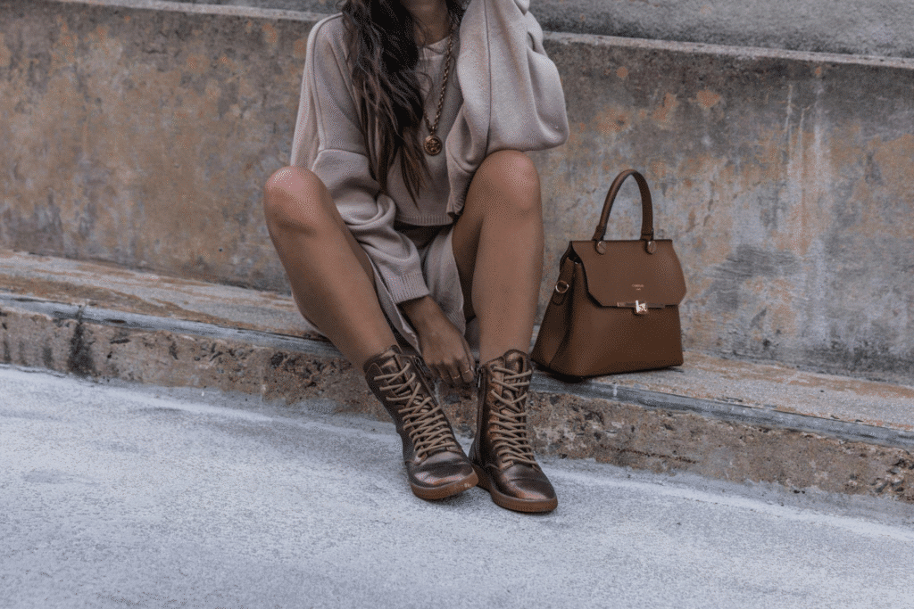 image Fashionable woman in a beige outfit with brown boots and matching handbag sitting against a rustic stone wall. | Sky Rye Design Fashionable woman in a beige outfit with brown boots and matching handbag sitting against a rustic stone wall.