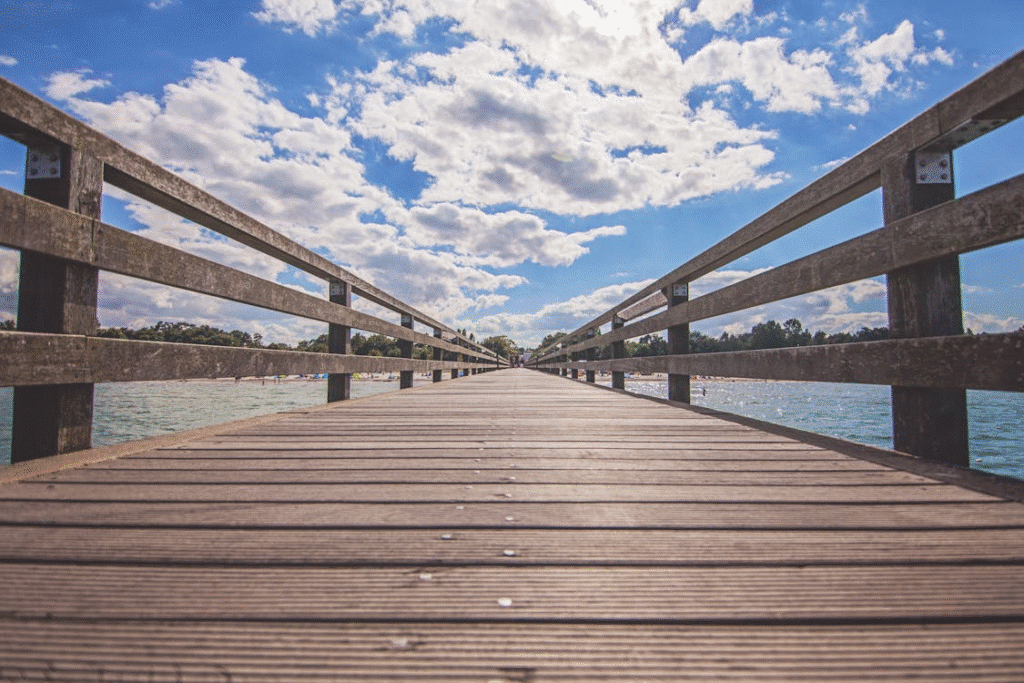 image Wooden pier extending over serene lake under a vibrant blue sky with fluffy clouds. | Sky Rye Design Wooden pier extending over serene lake under a vibrant blue sky with fluffy clouds.