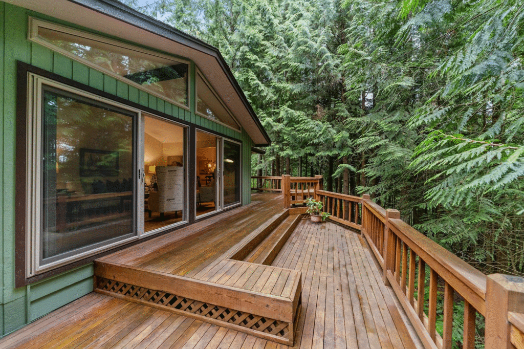 Wooden deck with forest view attached to a cozy cabin, featuring large glass doors opening to the inviting interior space.